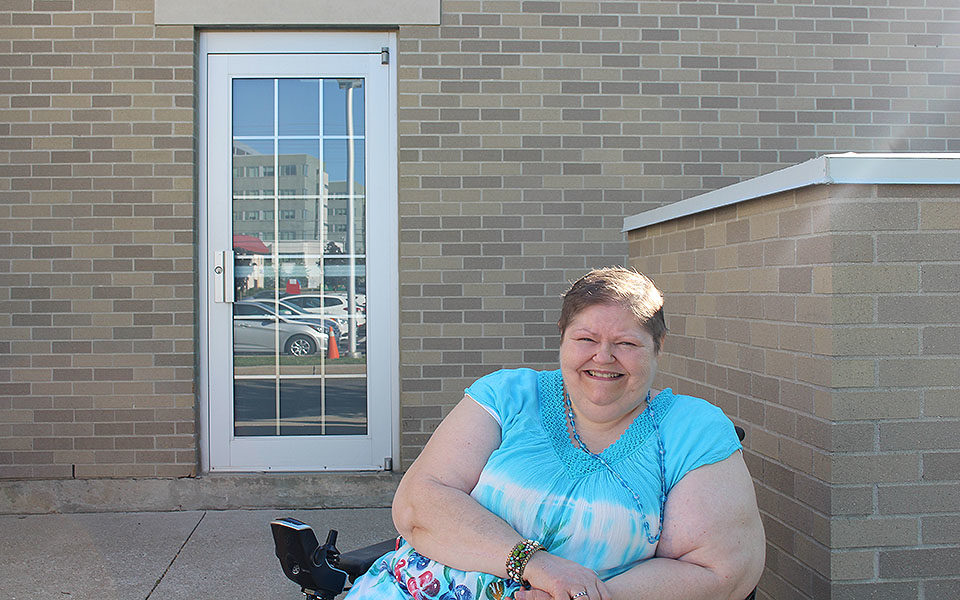 A woman in a wheelchair smiles outside of a brick building.